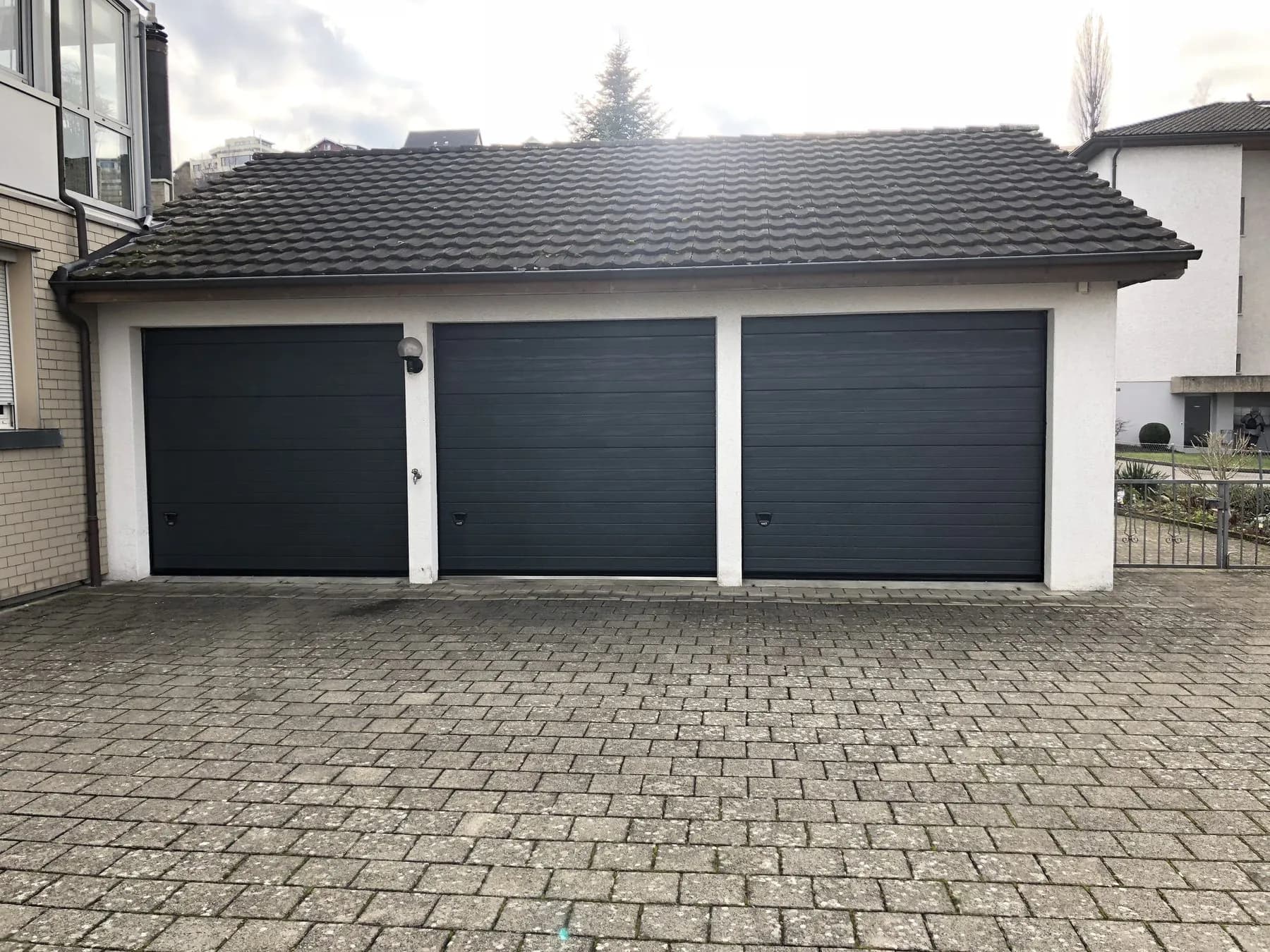 Drei anthrazitfarbene Sektionaltore nebeneinander an einer Garagenzeile