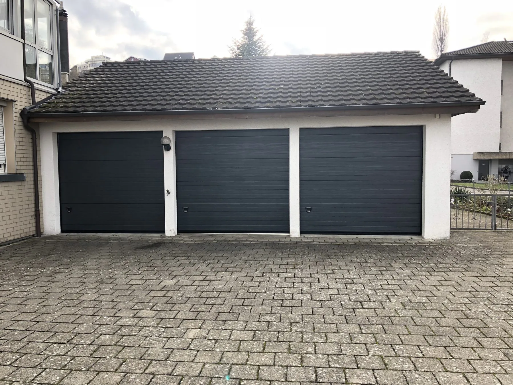 Drei anthrazitfarbene Sektionaltore nebeneinander an einer Garagenzeile